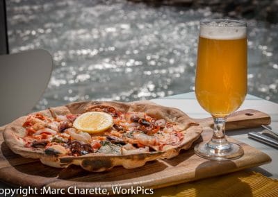 Commercial photography of waterfront restaurant with seafood pizza and beer on table