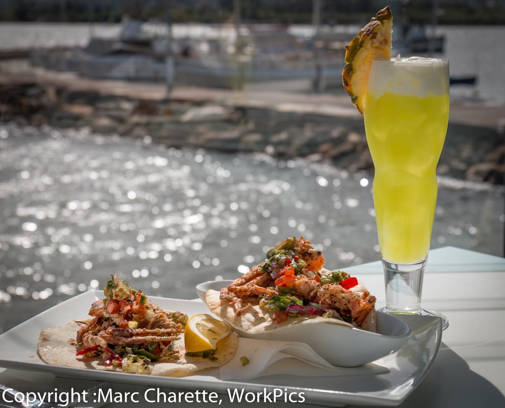 Commercial photography of waterfront restaurant with plated seafood and cocktail and water views