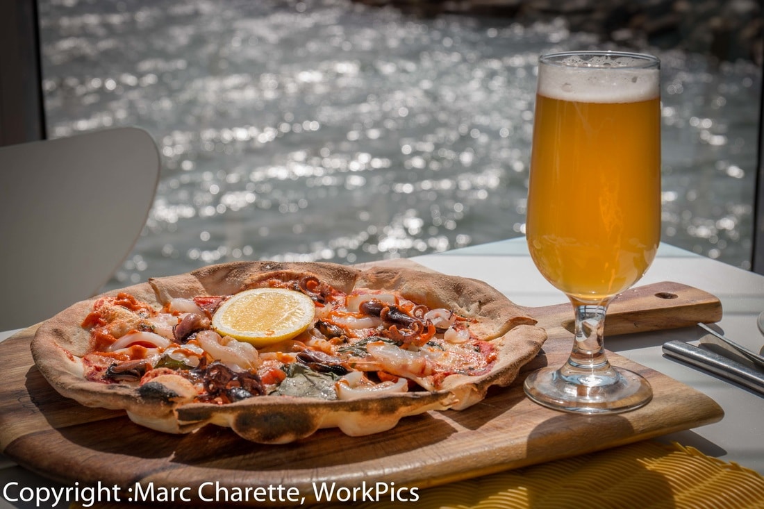 Commercial photography of waterfront restaurant with seafood pizza and beer on table